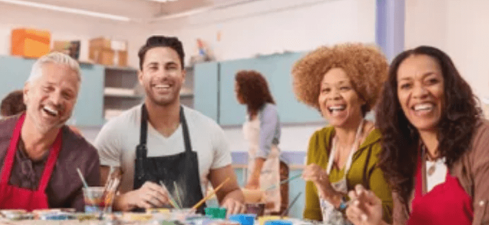 A man and woman sitting at a table with paint brushes.