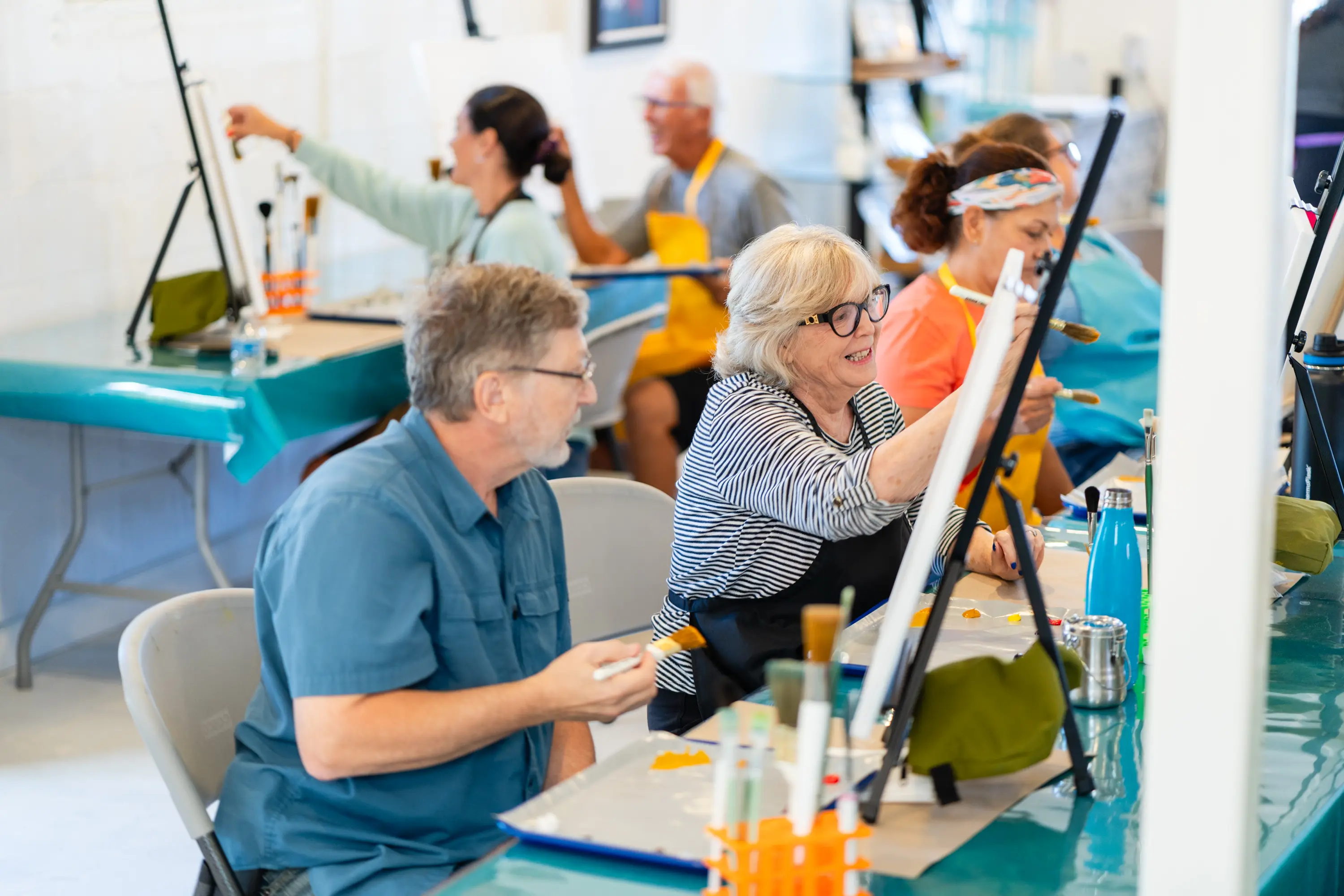 A group of people sitting at tables with paintings.