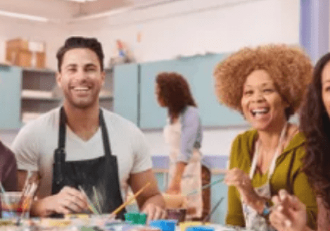 A man and woman sitting at a table with paint brushes.